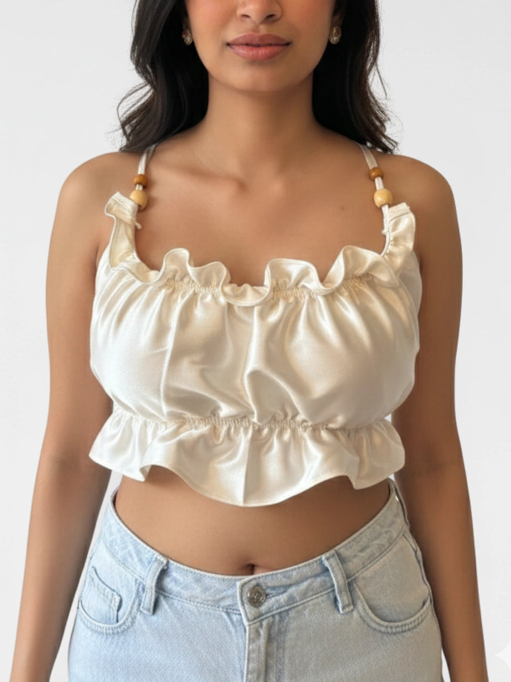 Woman wearing a cream-colored ruffled top with light blue jeans on a plain background