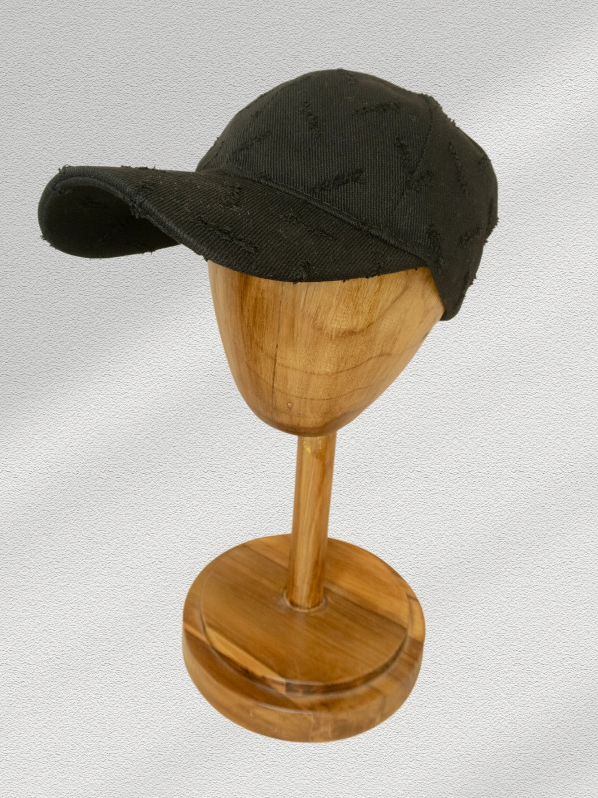 Black cap on a wooden mannequin head against a light gray background