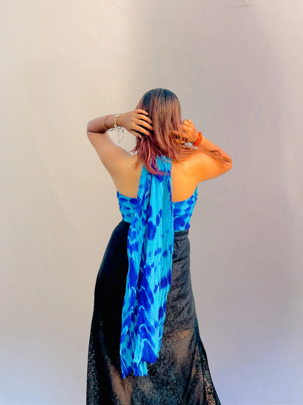 Person wearing a blue patterned scarf over a black outfit against a plain background