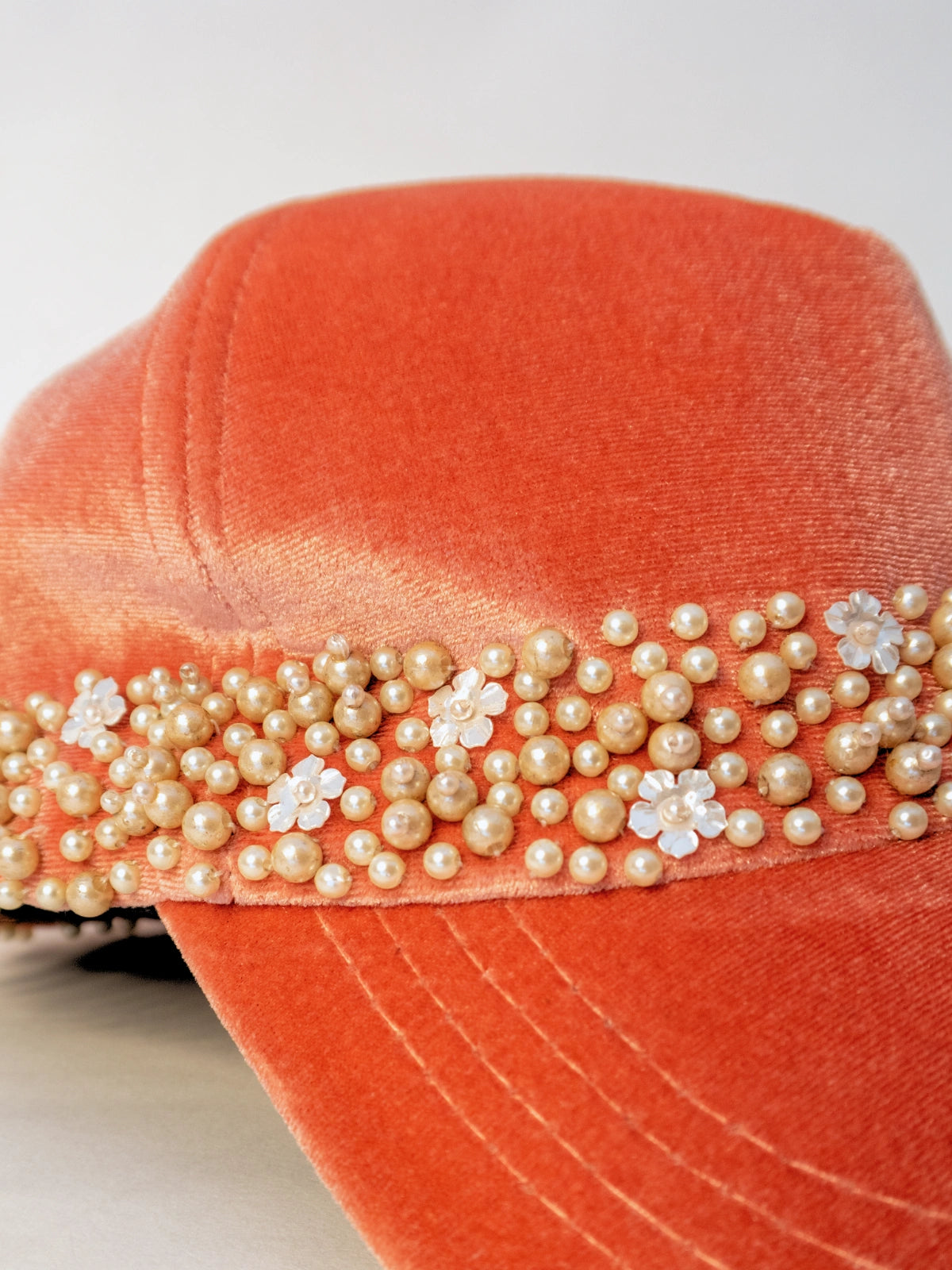 Orange hat with pearl and flower embellishments on a white background