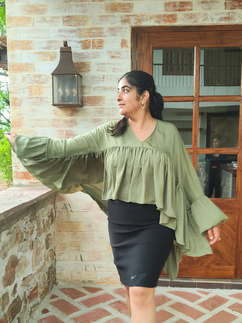 Woman wearing a green blouse and black skirt standing on a stone path.