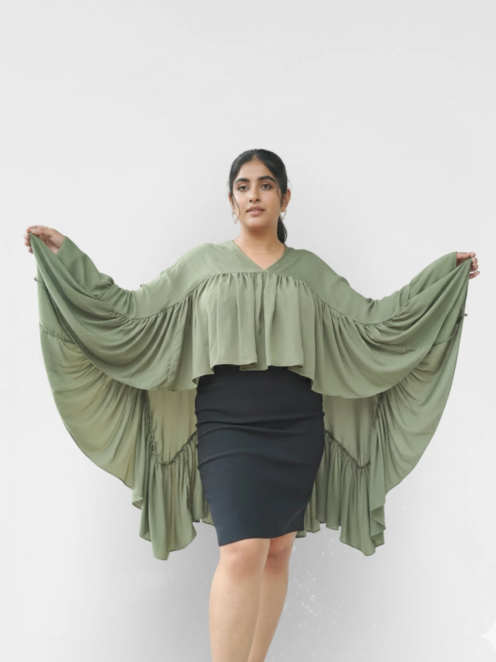 Woman wearing a green, flowing top with a plain background