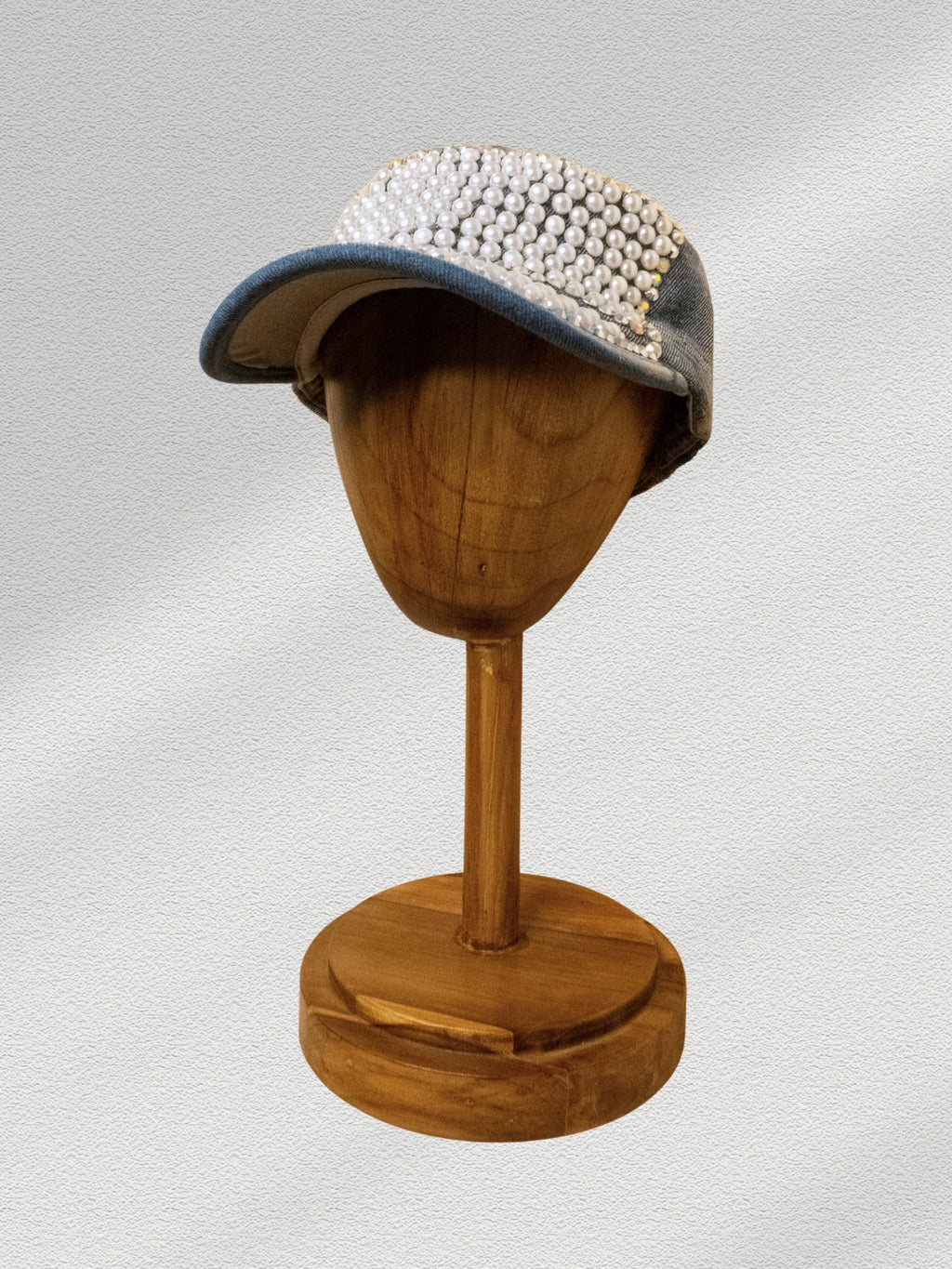 Cap with pearl embellishments on a wooden mannequin head against a light gray background