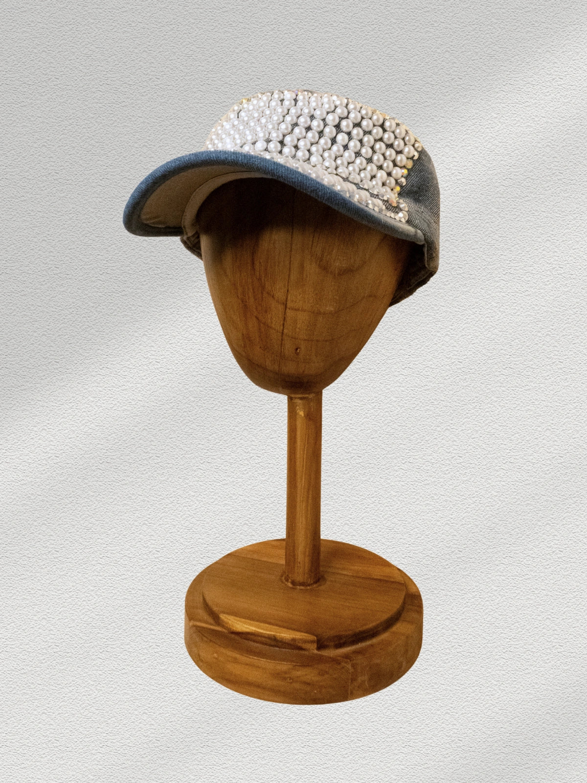 Cap with pearl embellishments on a wooden mannequin head against a light gray background