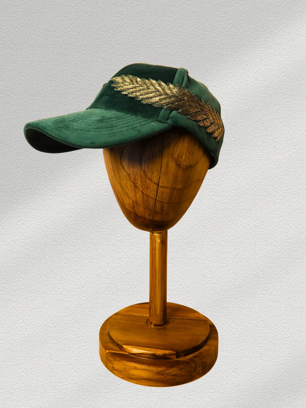Green cap with gold feather on a wooden mannequin head against a gray background
