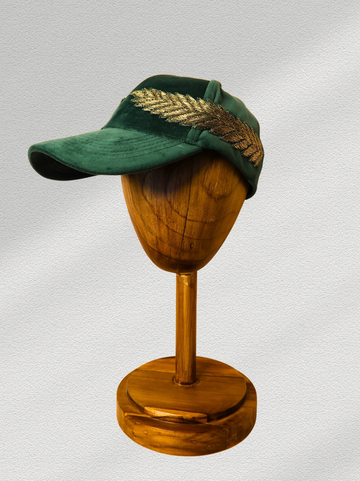 Green cap with gold feather on a wooden mannequin head against a gray background