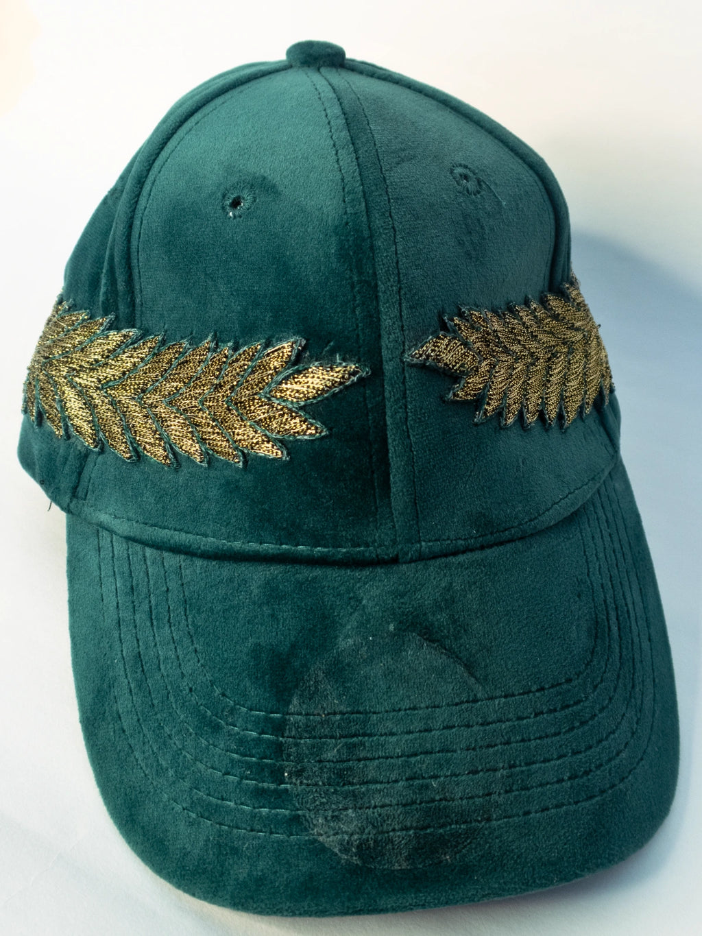 Green cap with gold leaf designs on a white background