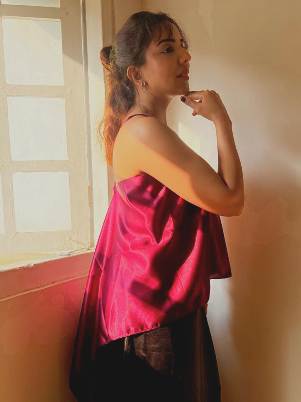 Woman wearing a red satin top standing in a room with a window.