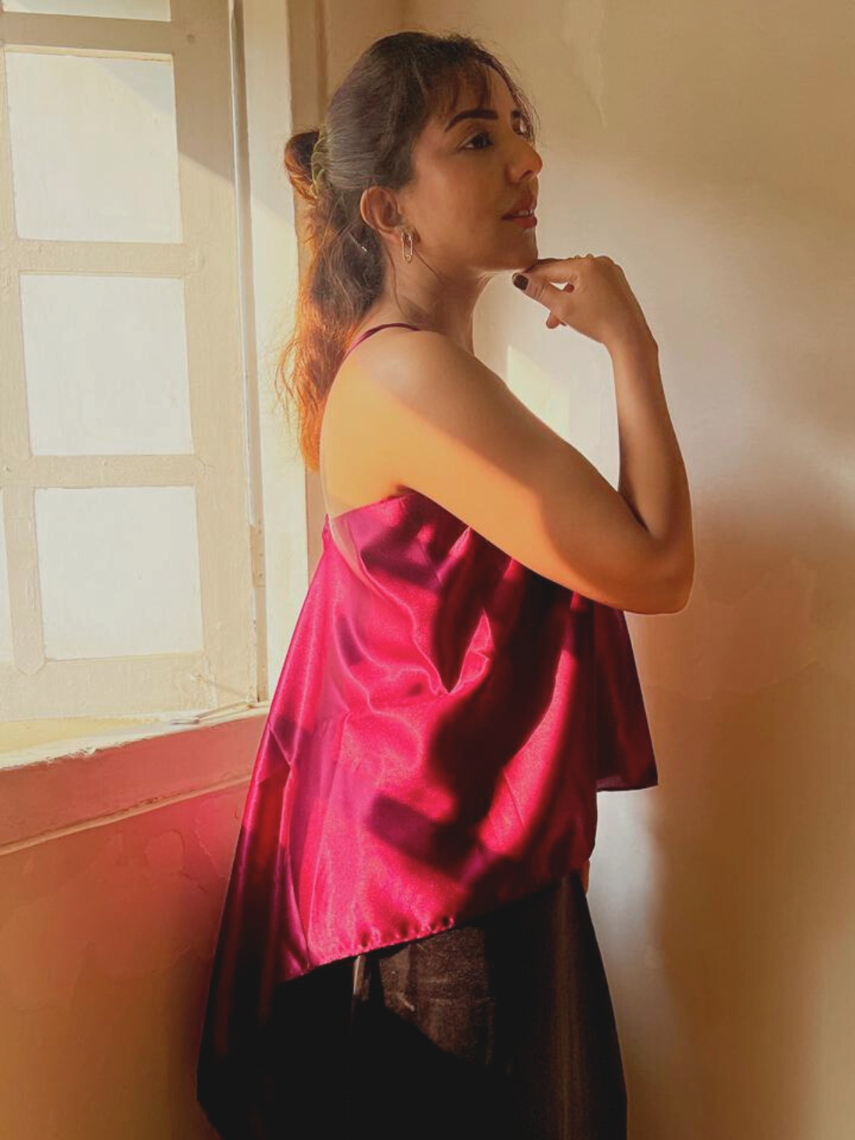 Woman wearing a red satin top standing in a room with a window.