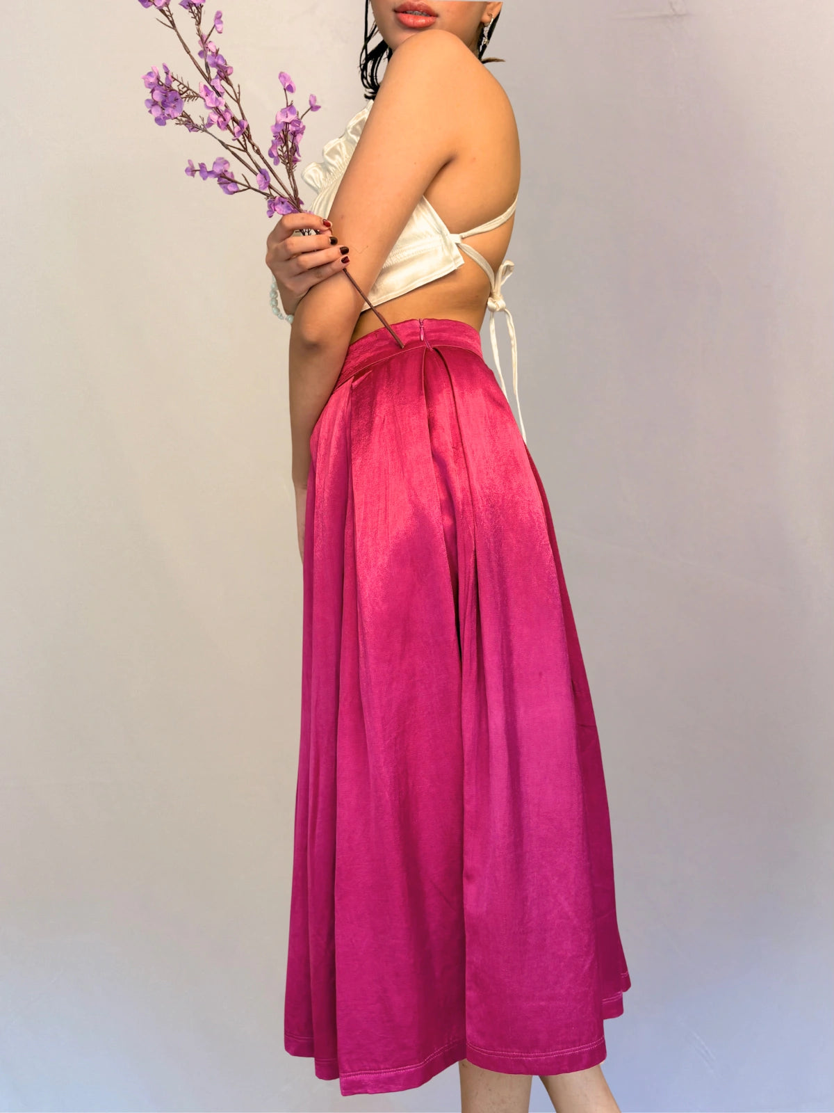 Person wearing a white top and pink skirt holding purple flowers against a plain background