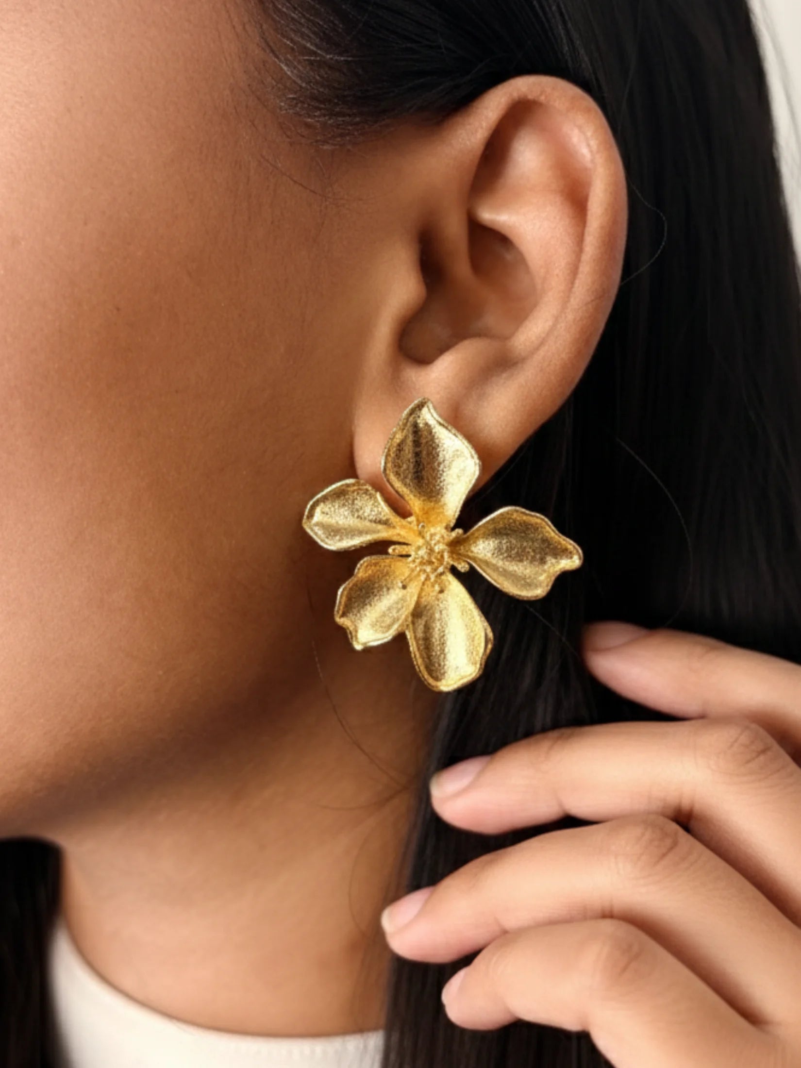 Gold flower-shaped earring worn by a person with dark hair.