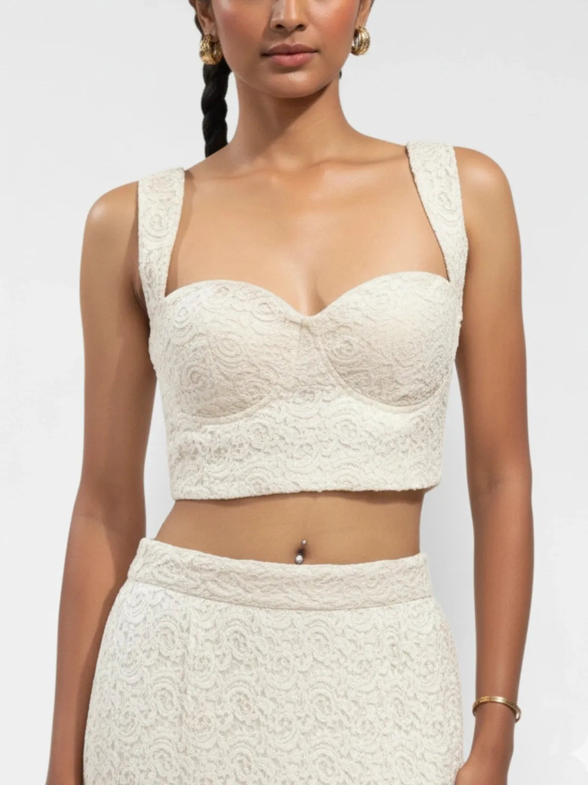 Woman wearing a white lace top and skirt set against a plain background