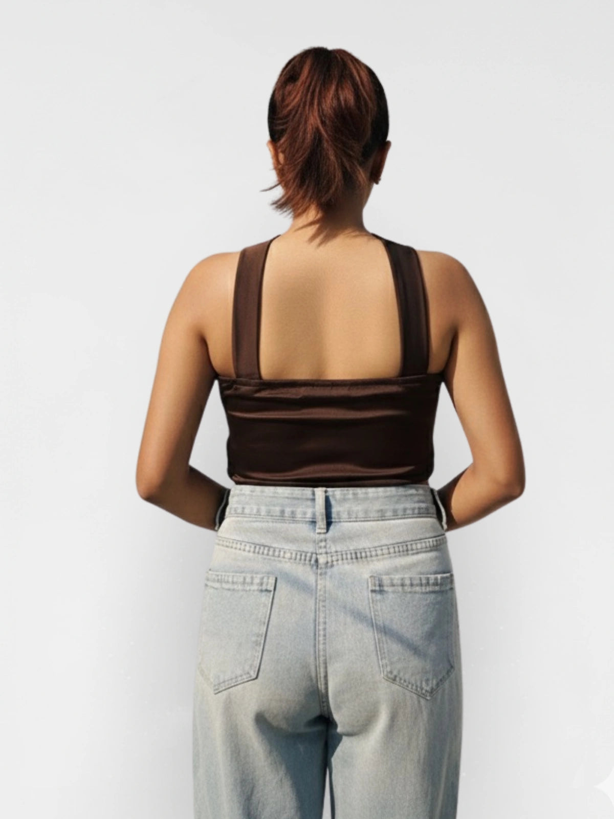 Person wearing a brown tank top and light blue jeans on a white background