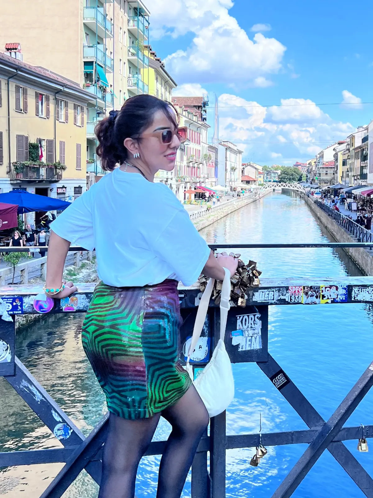 Woman standing by a canal with buildings and people in the background