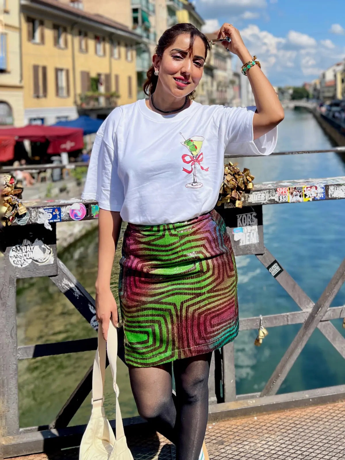 Woman standing on a bridge over a canal with colorful skirt and white t-shirt.