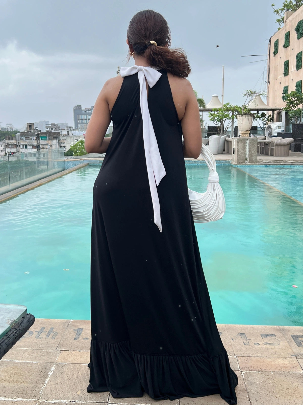 Woman in a black dress with a white bow standing by a poolside.