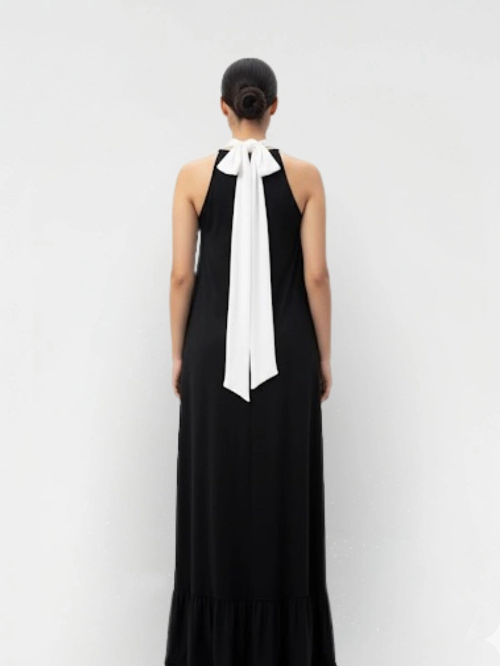 Black dress with a white bow detail on a plain background