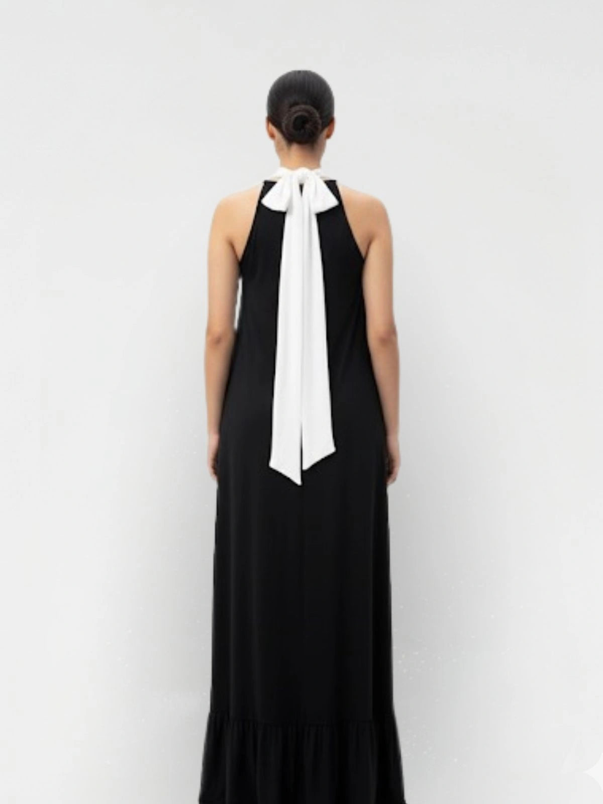 Black dress with a white bow detail on a plain background