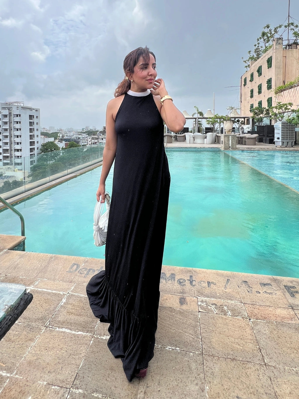 Woman in a black dress standing by a pool with buildings in the background