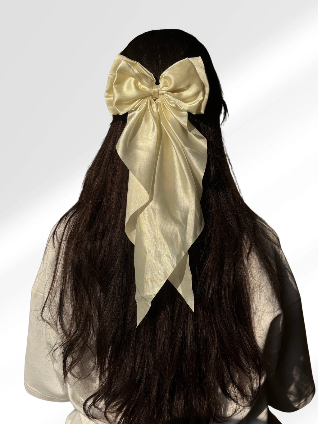 Mannequin head with long dark hair styled with a large beige bow on a white background