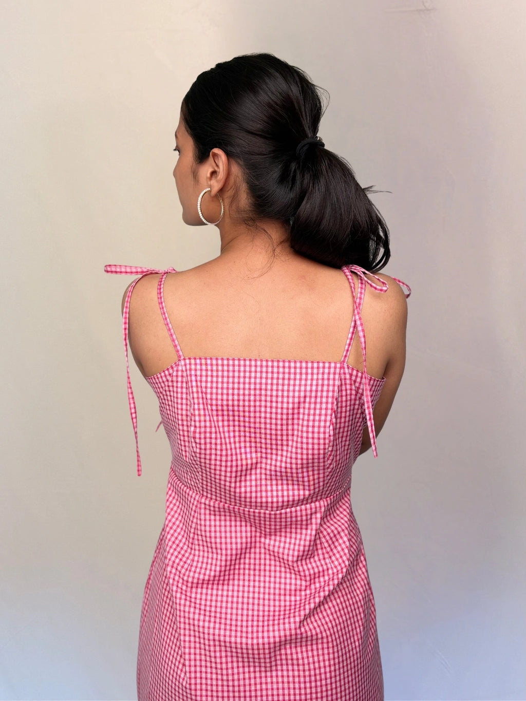Woman wearing a pink checkered dress with thin straps against a plain background