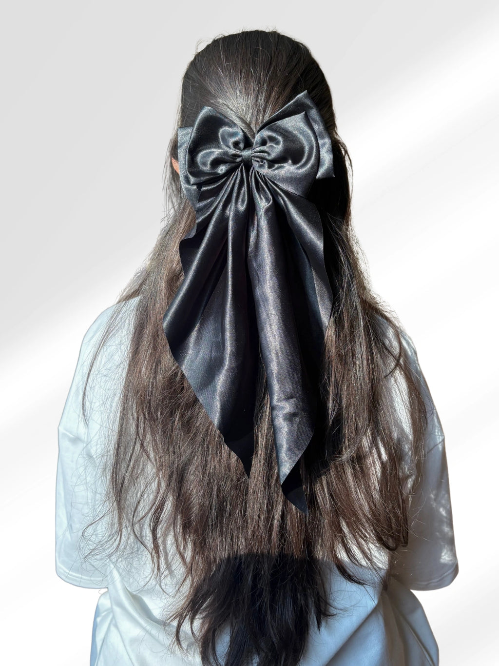 Person with long hair wearing a large black bow on a white background