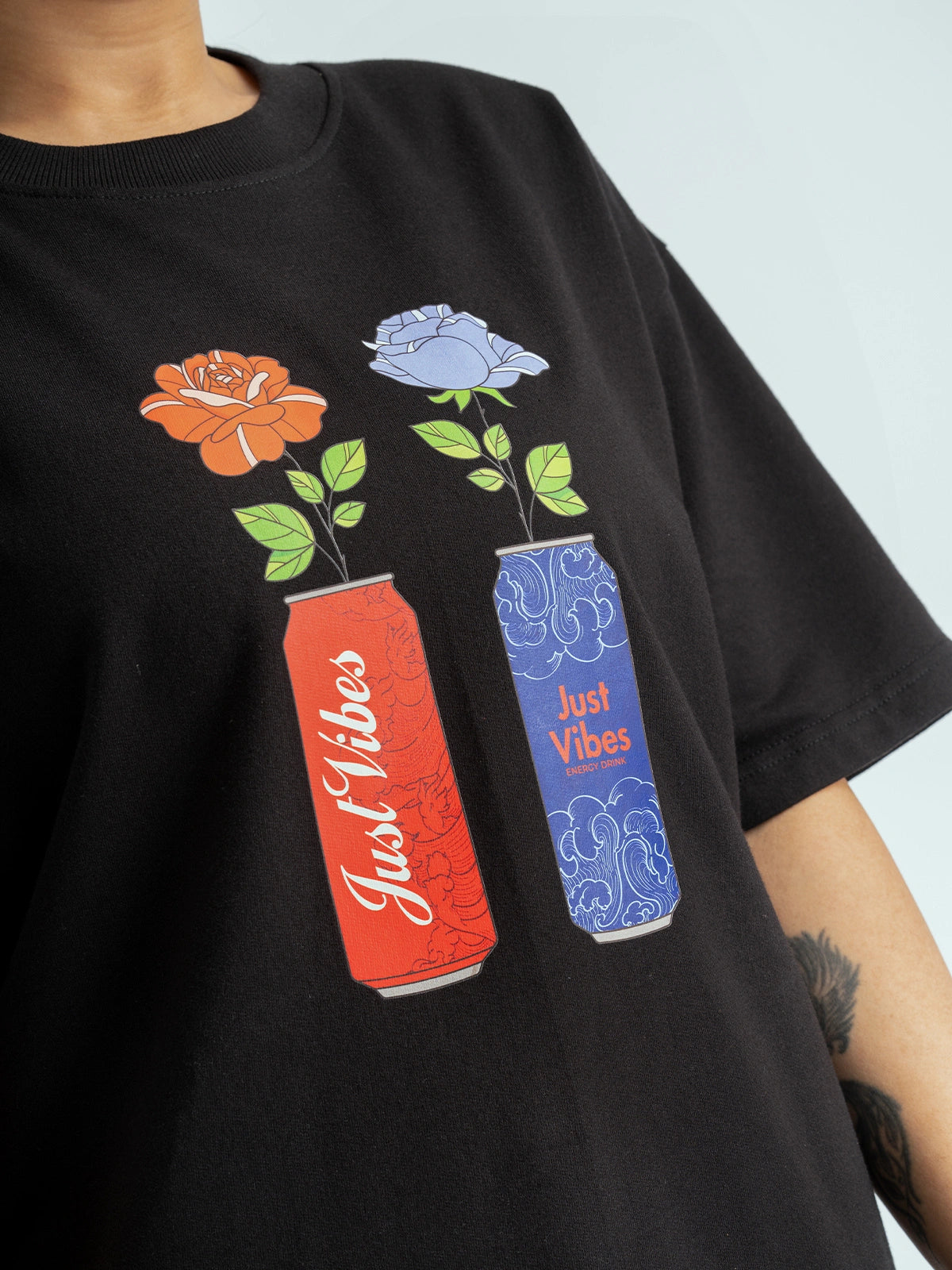 Black t-shirt with 'Just Vibes' cans and flowers design on a light blue background