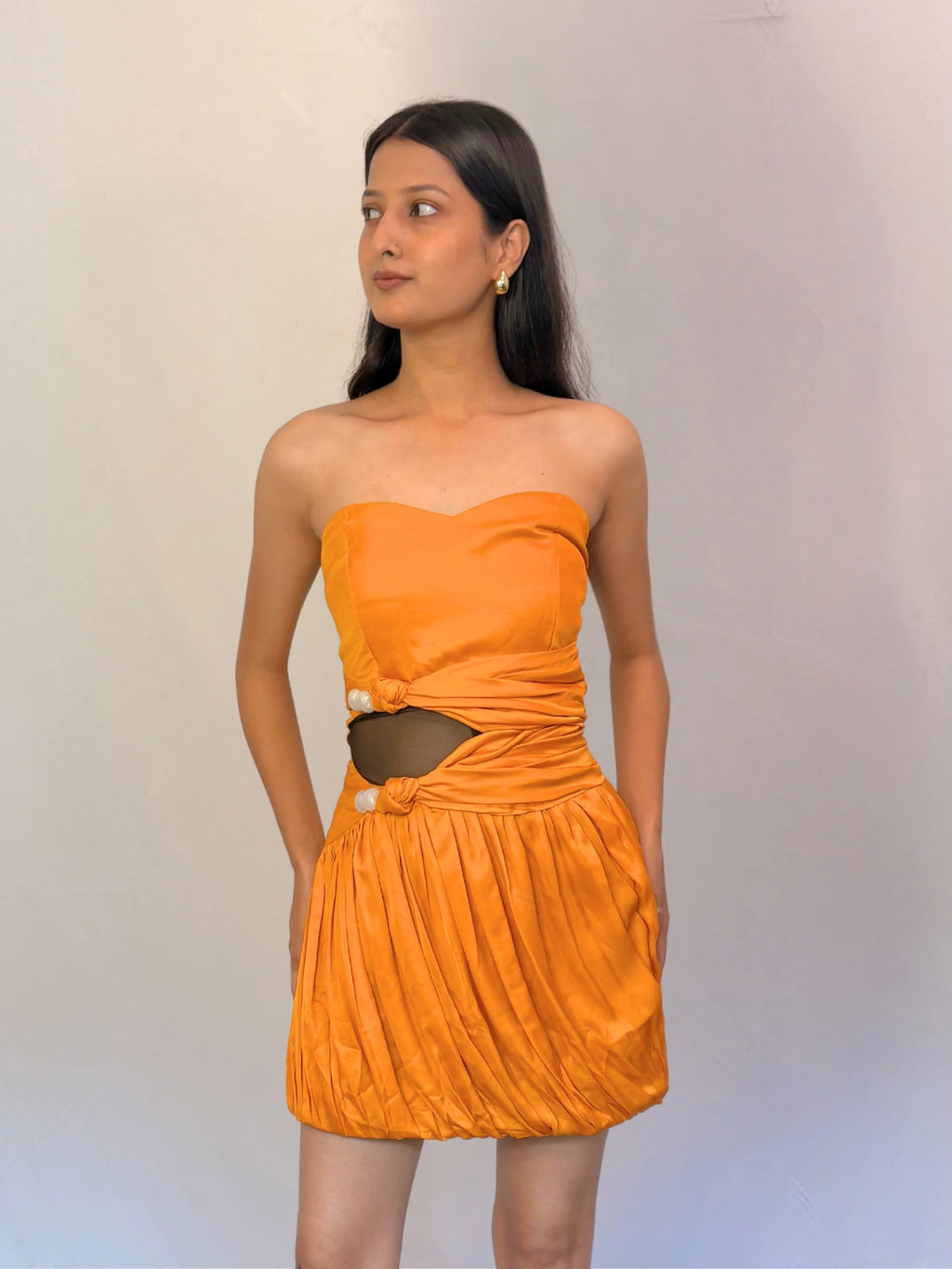 Woman wearing an orange strapless dress with a cutout design on a plain background