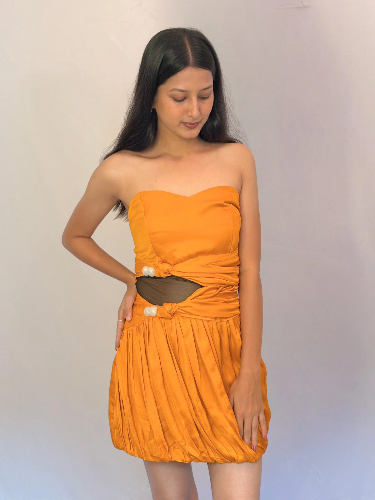 Woman wearing an orange strapless dress with cut-out design against a plain background