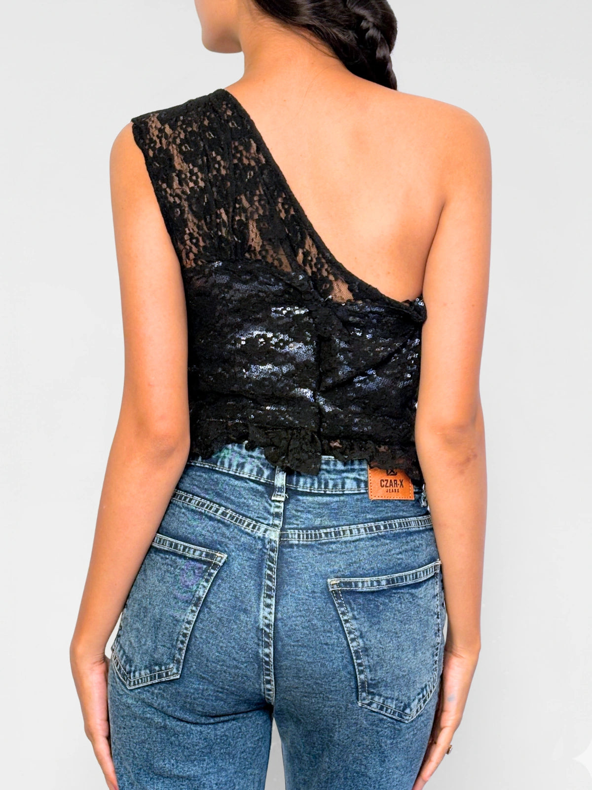 Person wearing a black lace top and blue jeans on a plain background
