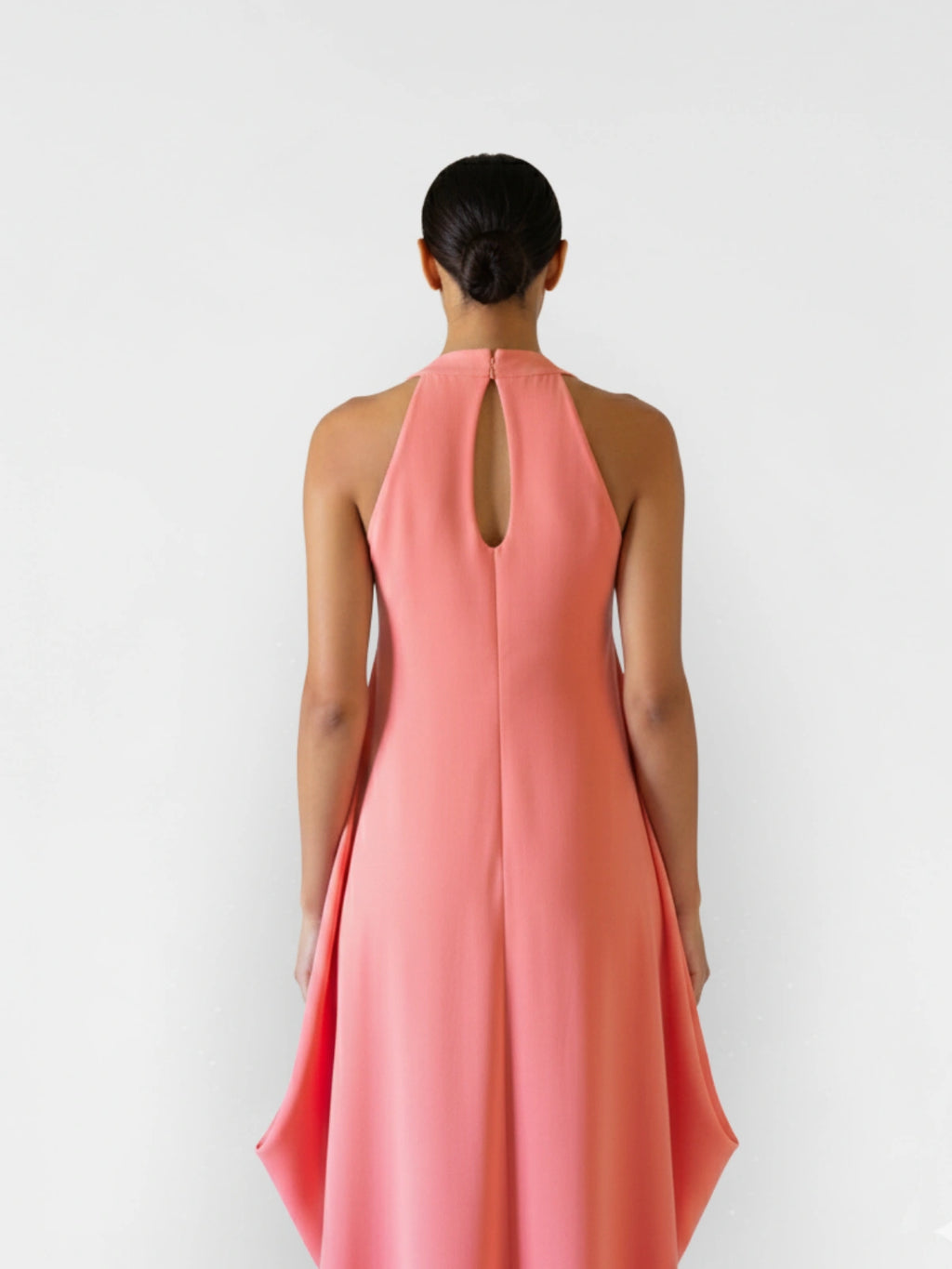 Woman wearing a coral pink dress with a halter neck design on a white background