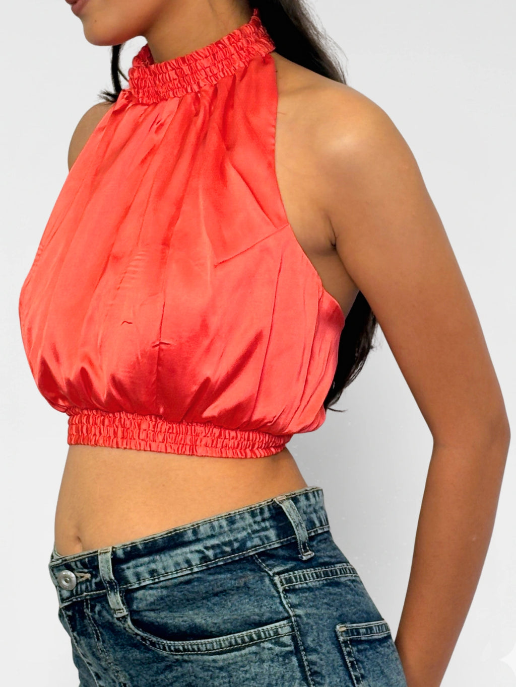 Person wearing a coral halter top and blue jeans on a plain background