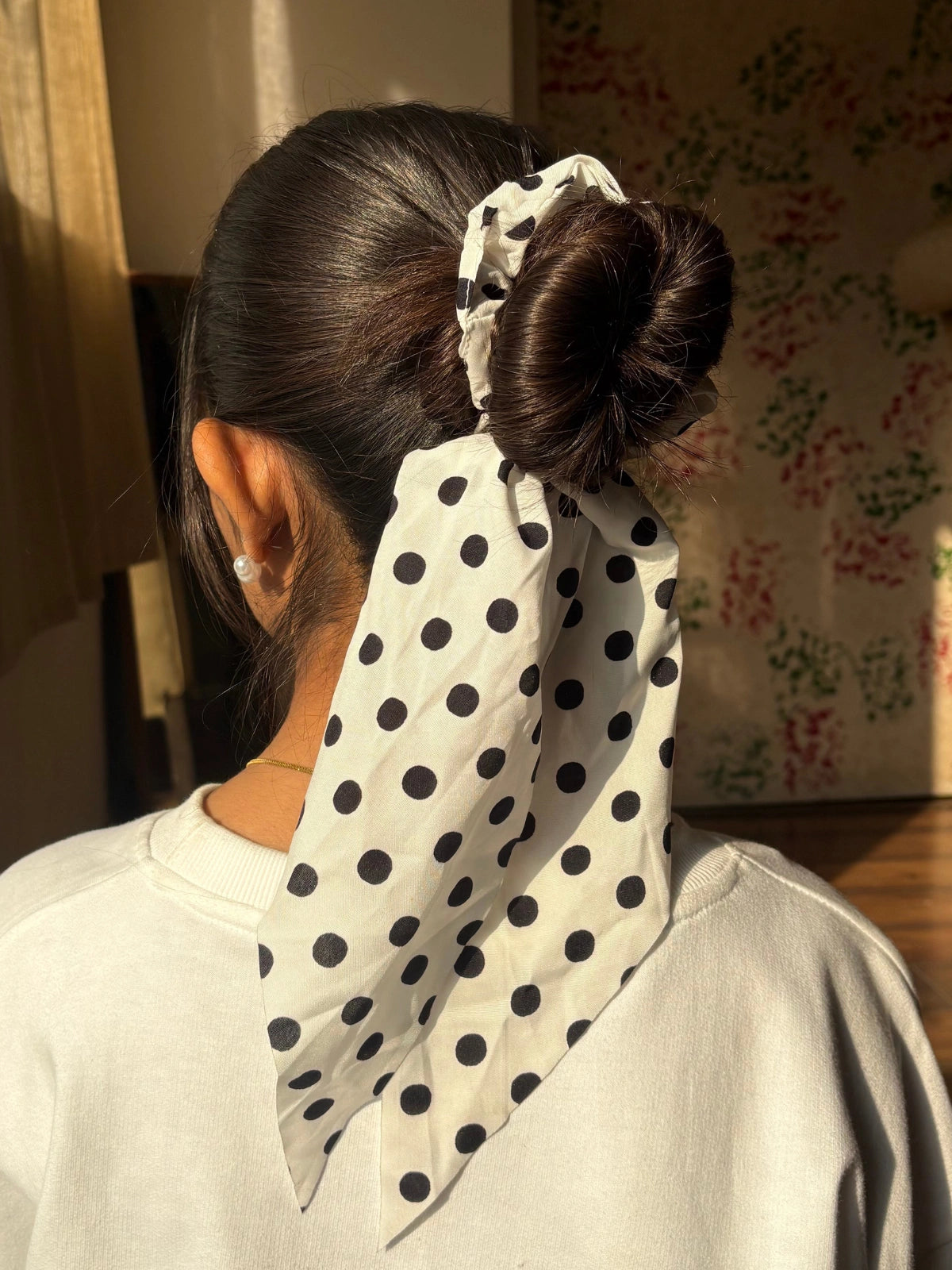 Person with a polka dot headscarf tied in a bun, wearing a light-colored top.