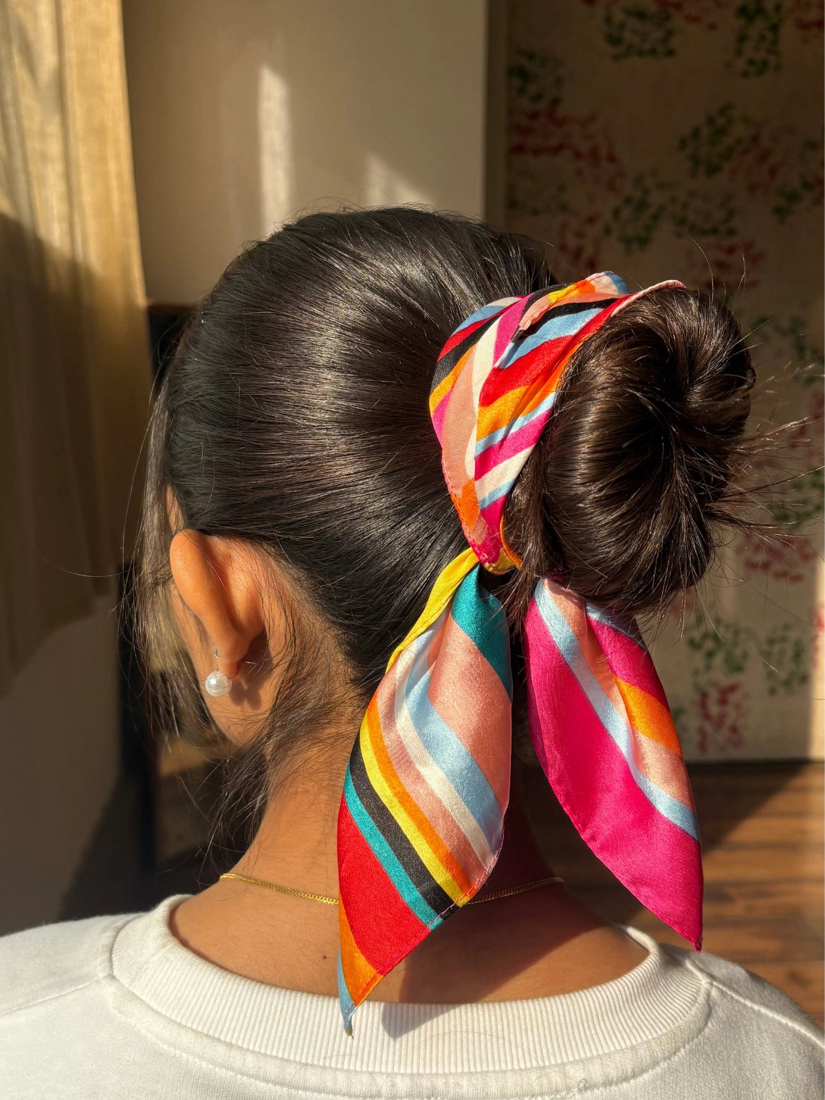 Person with a colorful headscarf tied in a bun, standing indoors.